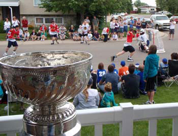 Kris Versteeg along with friends enjoying a street hockey game while the Stanley Cup looks on.