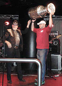 Antti Niemi proudly hoisting the Stanley Cup on stage with a musician at a local drinking establishment