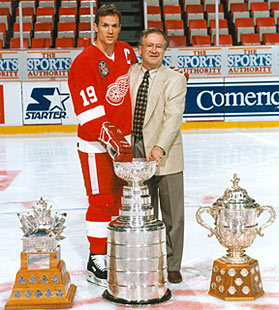Jim Devellano and Steve Yzerman along with the Conn Smythe Trophy, The Stanley Cup and the Clarence S. Campbell Bowl.