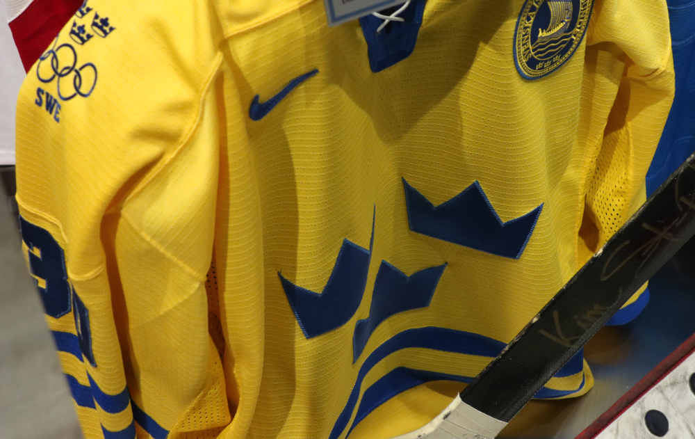 Gold medal awarded to Canada and the 2002 Olympic Winter Games is shown in the right forefront. Jersey worn by Geraldine Heaney (<i>HHOF 2013</i>) and stick used by Jocelyne Lamoureux are seen in the background.